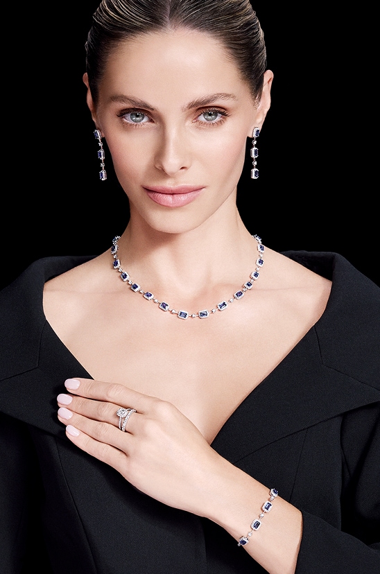 A model in a black dress presenting a jewellery set with emerald-cut blue sapphire and diamonds