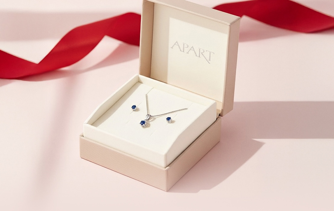A box with the Apart logo, containing earrings and a cubic zirconia chain.
