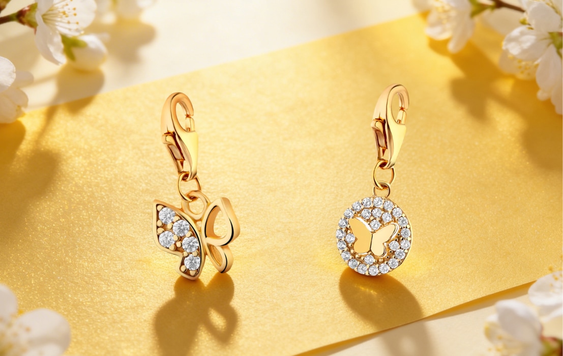 Two gold pendants from the charms collection with a butterfly motif on a yellow background with white flowers