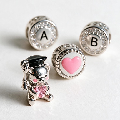 Silver bracelet charms featuring the letters A and B, a pink heart, and a teddy bear charm with a pink crystal