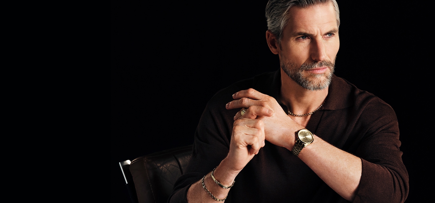 A man against a black background, showcasing gold jewelry and a watch