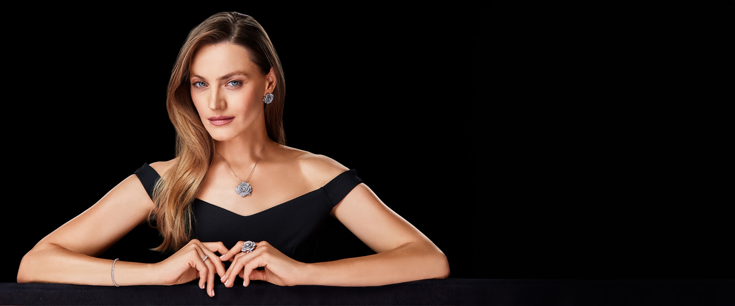 A model in a black dress showing off silver jewellery - a necklace, earrings, a ring, and a bracelet with a floral motif