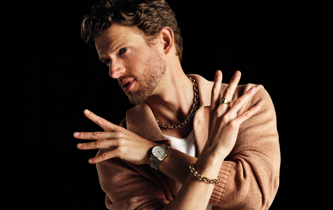 A man in a beige sweater showing off a set of jewelry and a men's watch
