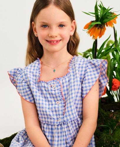 Smiling girl in a checkered dress. Showing off gold earrings and an enamel necklace