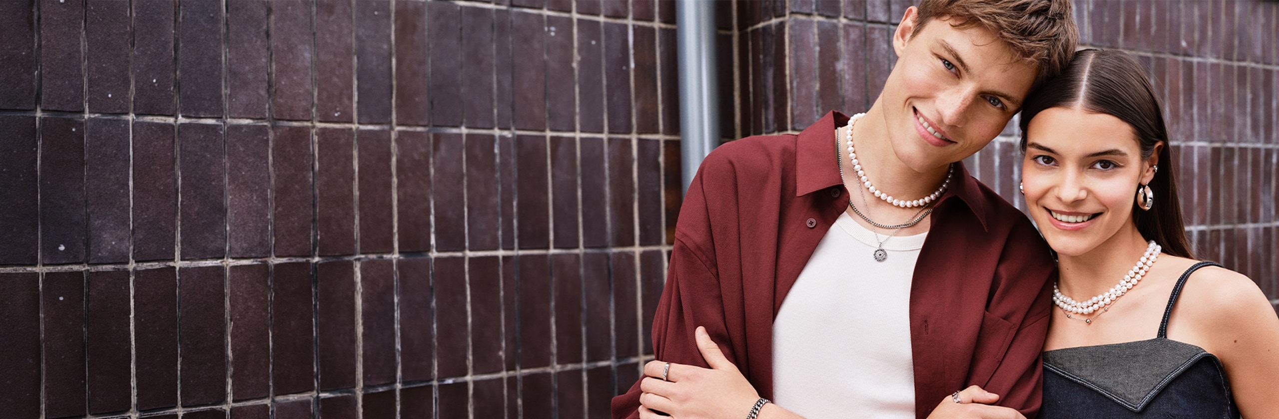 A pair of young teenagers showcase elegant jewelry while standing together against an urban backdrop
