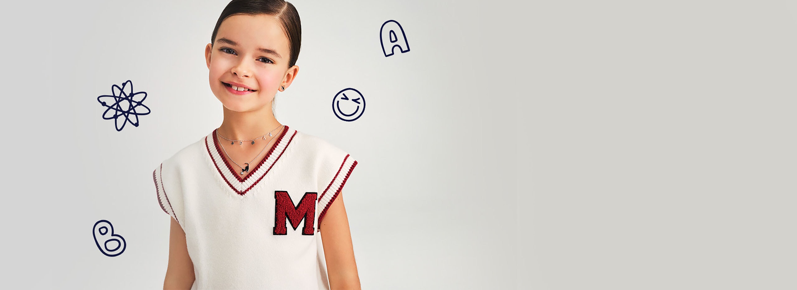 uśmiechnięta dziewczynka ubrana w beżowy sweterek prezentuje kolczyki i naszyjnik