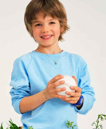 Uśmiechnięty chłopiec trzymający w rękach białą piłkę do baseball. Prezentuje biżuterię dla najmłodszych