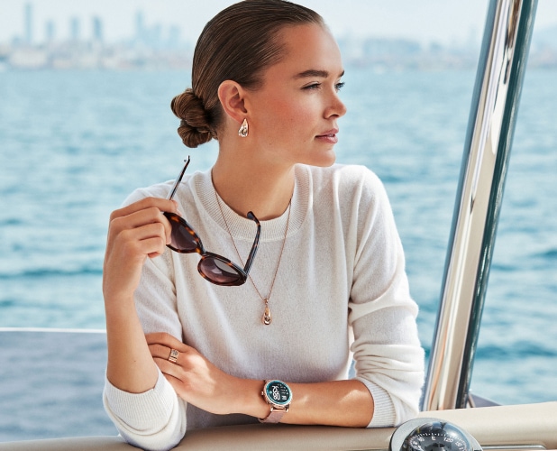 Zosia Nowak, with the sea in the background, presenting Elixa brand products - earrings, glasses, a necklace, a ring and a watch