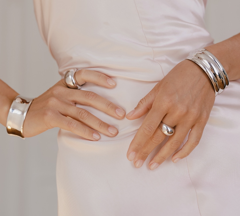 Modelka prezentuje srebrne pierścionki i bransoletki o wyrazistych, ekspresyjnych formach