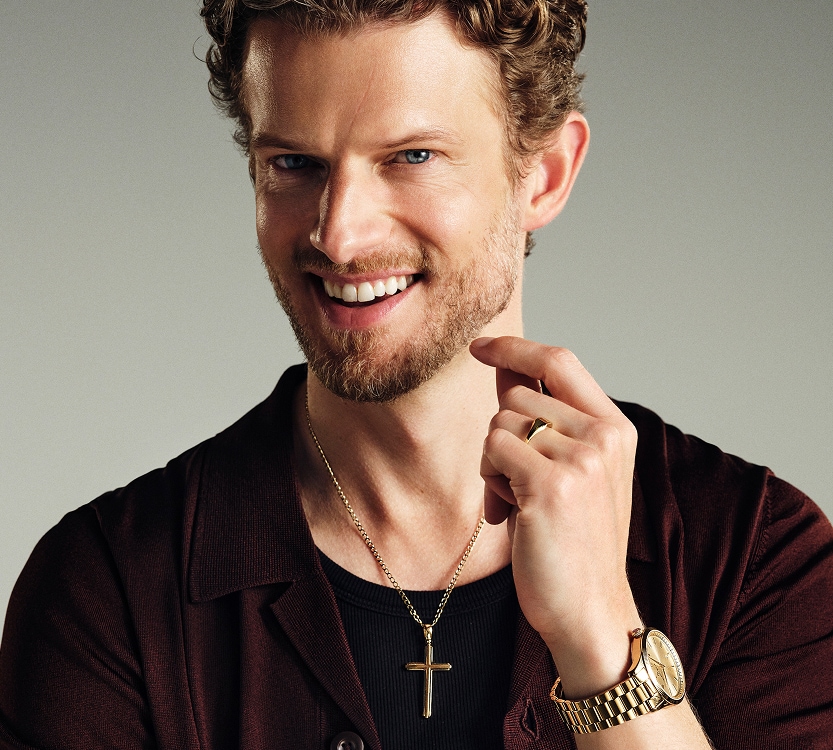 Mężczyzna prezentujący złoty zegarek oraz złoty naszyjnik z zawieszką w kształcie krzyża