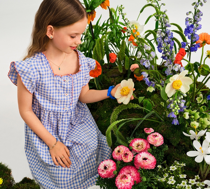 Dziewczynka w sukience w niebieską kratę patrząca na kwiaty