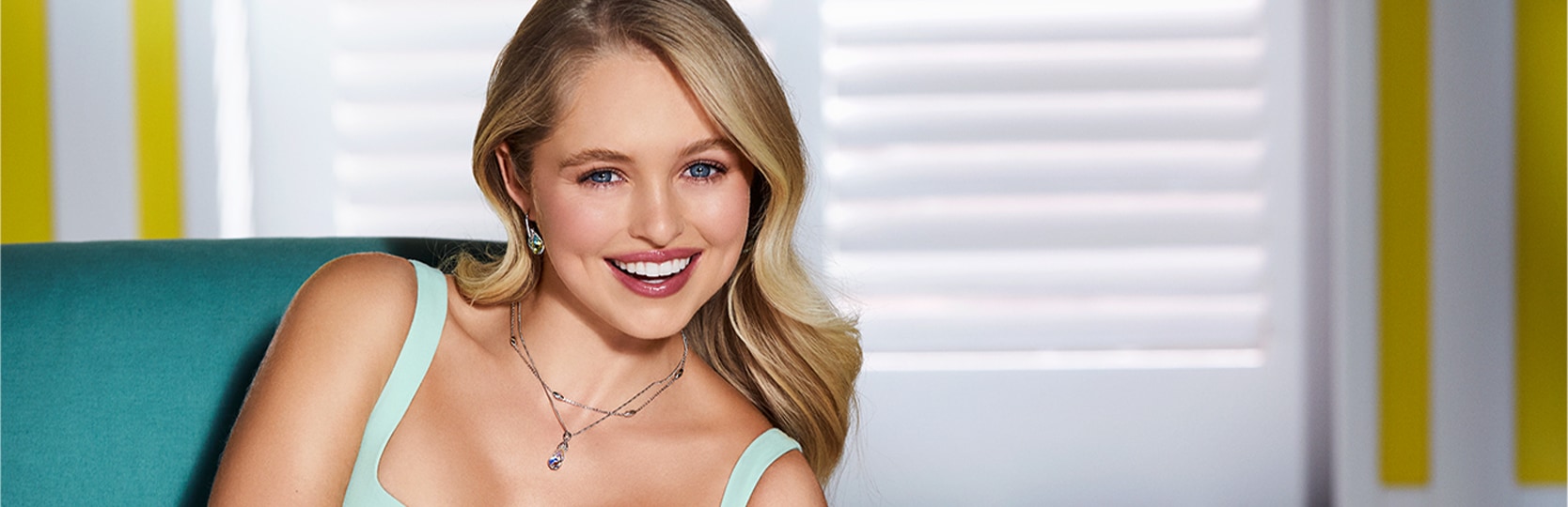 Kobieta o blond włosach w sukience w kolorze turkusowym prezentuje biżuterię