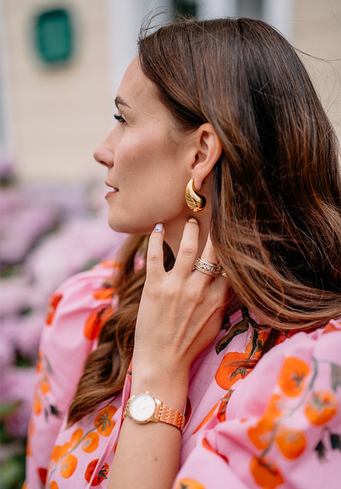 Kobieta prezentuje kolczyki pozłacane, pierścionki z diamnentami i zegarek