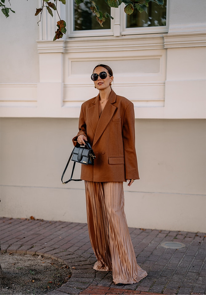 Kobieta ubrana w jesienną kreacje w brązowych odcieniach prezentująca biżuterię