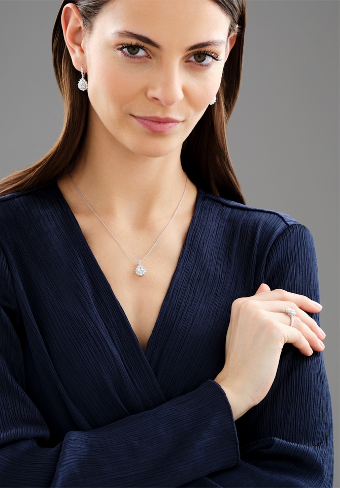 Kobieta w granatowej marynarce prezentująca kolczyki, łańcuszek z zawieszką oraz pierścionek z białego złota