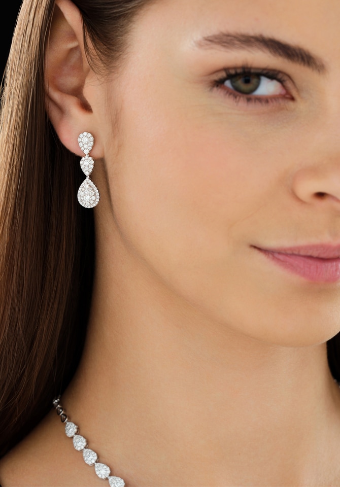 Kobieta w brązowych włosach prezentująca kolczyki oraz naszyjnik z białego złota