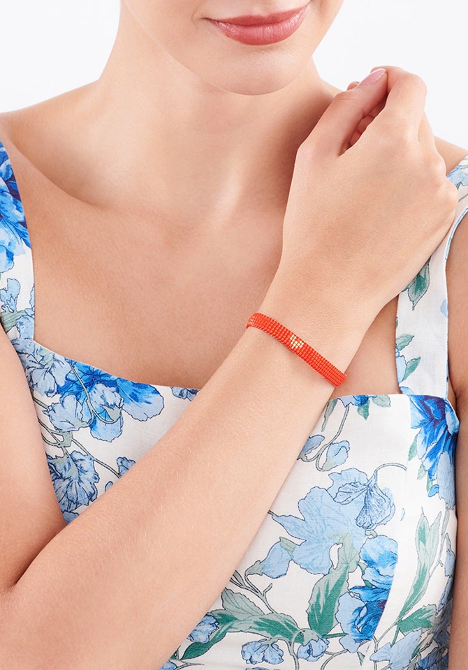 kobieta ubrana w białą suknie w niebieskie kwiaty prezentuje na nadgarstku bransoletke w kolorze czerwieni