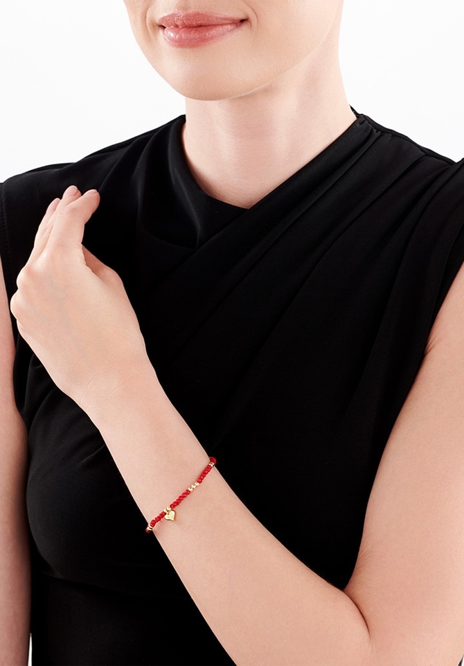 kobieta ubrana w czarną suknie prezentuje na nadgarstku bransoletke w kolorze czerwieni