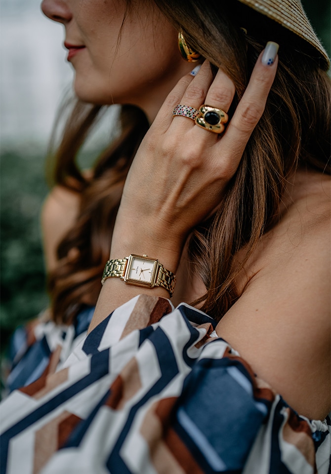 kobieta ubrana w białą koszule prezentuje komplet biżuterii złotej wraz z zegarkiem 