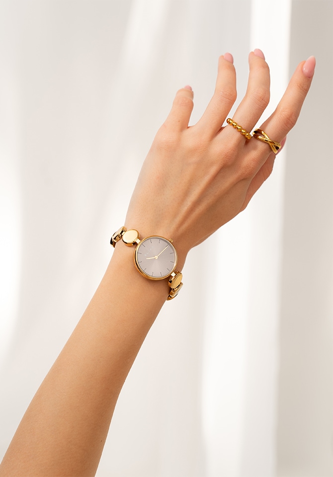 kobieta ubrana w białą koszule prezentuje komplet biżuterii złotej wraz z zegarkiem 