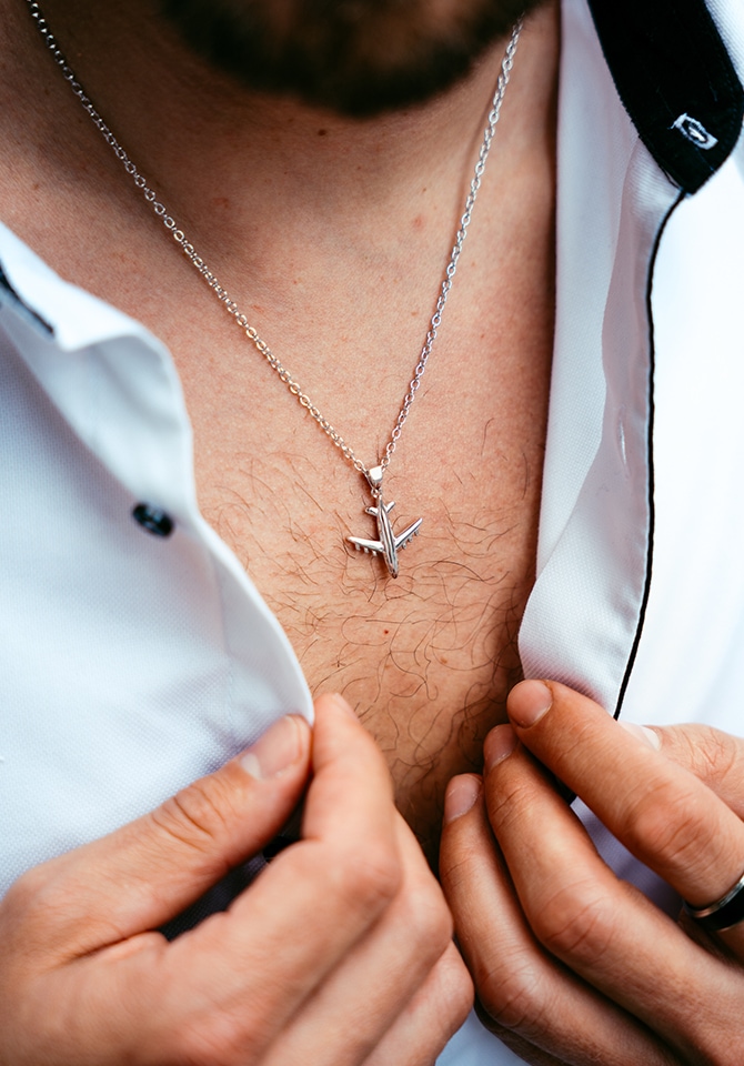 Mężczyzna w białej koszuli prezentujący srebrny naszyjnik z zawieszką - samolot