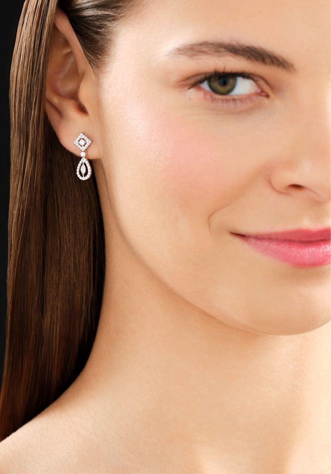 Kobieta prezentująca kolczyki z białego złota z diamentami założone na uszach