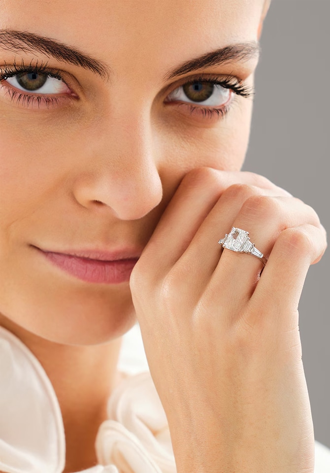 Kobieta ubrana w białą jedwabną koszulę prezentuje pierścionek z białego złota z diamentami założony na palcu