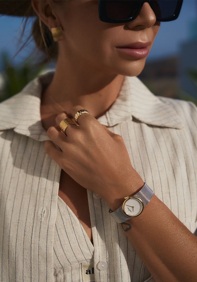 zegarek damski z bransoletą ze stali szlachetnej założony na nadgarstku oraz pierścionki złote założone na placach
