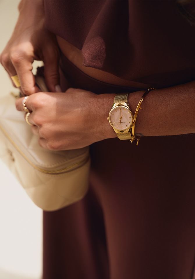 zegarek z bransoletą z mosiądzu oraz złota brnsoletka założone na nadgarstku kobiety
