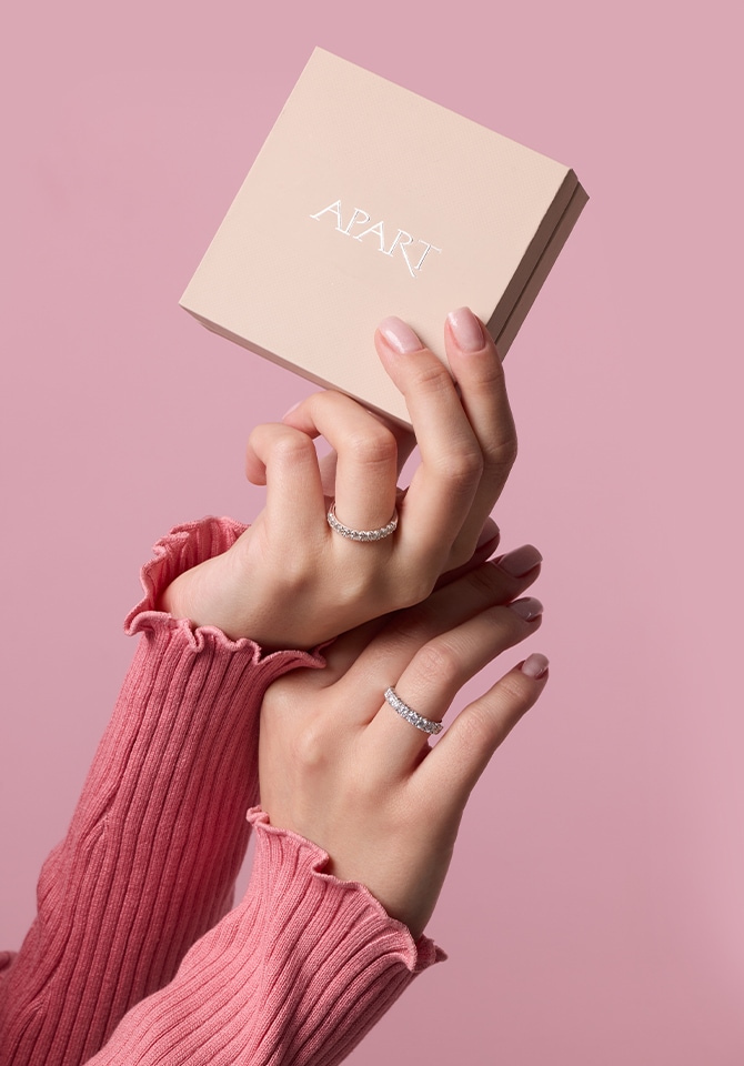 Kobieta prezentująca pierścionki na palcach. Trzyma w dłoni pudełko na biżuterię Apart