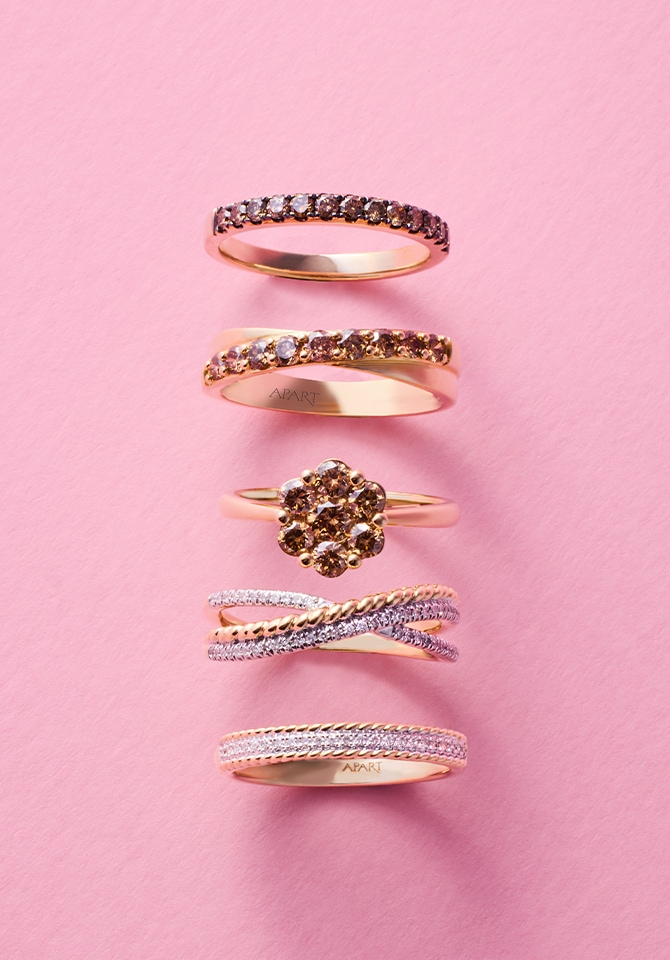 Kilka złotych pierścionków ułożonych w rzędzie na różowym tle