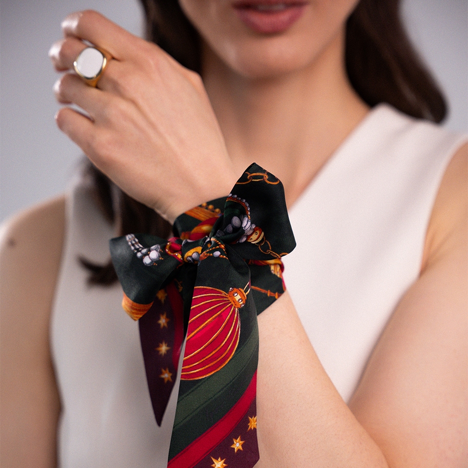 Modelka prezentująca przewiązaną na nadgarstku jedwabną apaszkę o świątecznym wzorze