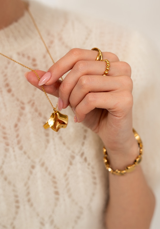 Kobieta prezentująca pozłacane pierścionki na palcach oraz naszyjnik z zawieszką 