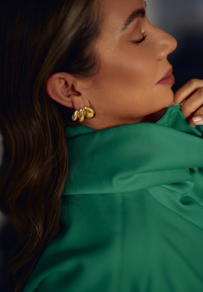 Modelka ubrana w płaszcz w kolorze butelkowej zieleni w stylizacji złotej biżuterii