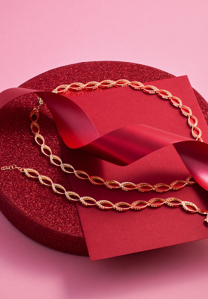 Złote bransoletki z diamentami położone na czerwonej połyskującej okrągłej podstawce