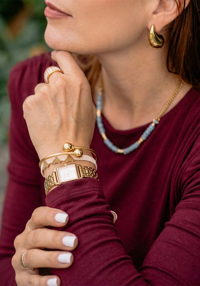 Kobieta prezentuje kolczyki pozłacane, bransoletki oraz zegarek