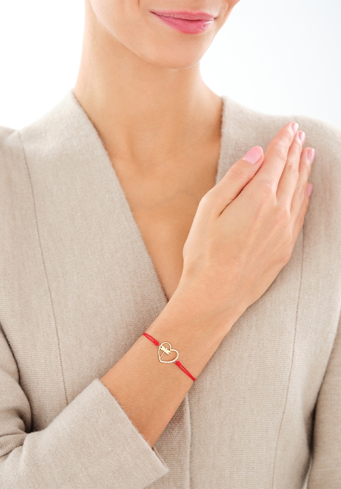 Kobieta prezentująca bransoletkę na czerwonym sznurku z elementem ze złota - serce