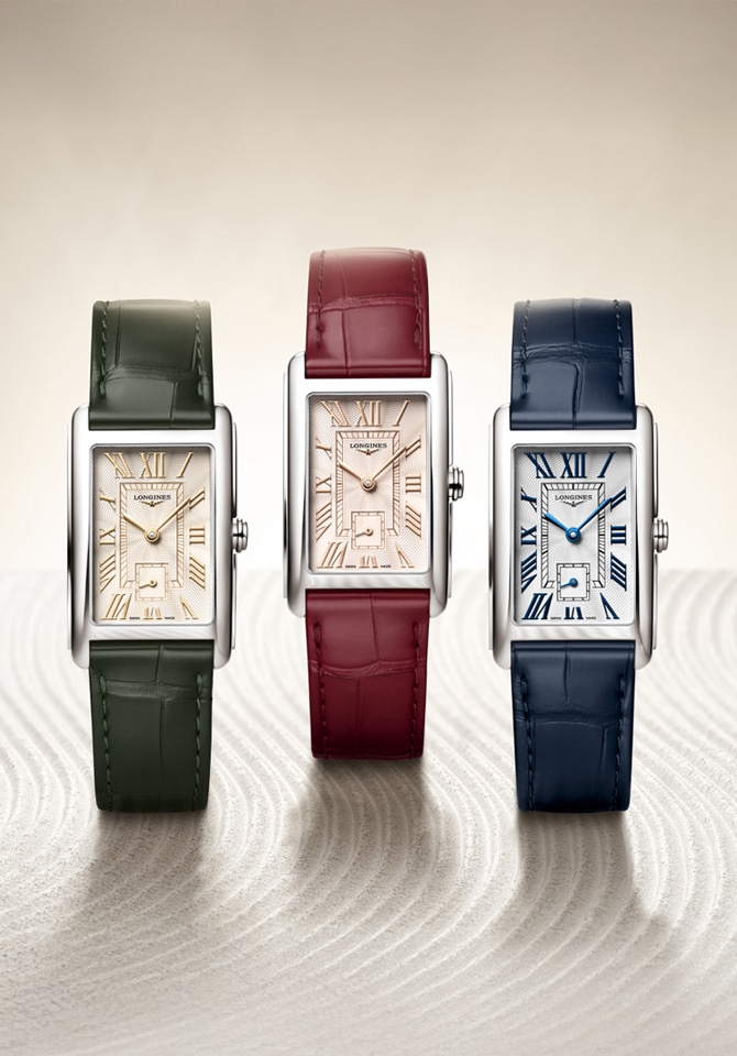Trzy prostokątne zegarki Longines z jasnymi tarczami i skórzanymi paskami w kolorach zielonym, bordowym i granatowym, prezentowane na jasnym tle