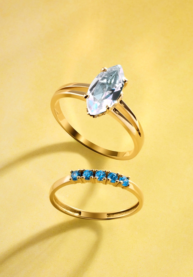 Złote pierścionki z diamentem i niebieskimi kamieniami szlachetnymi – elegancka biżuteria na żółtym tle