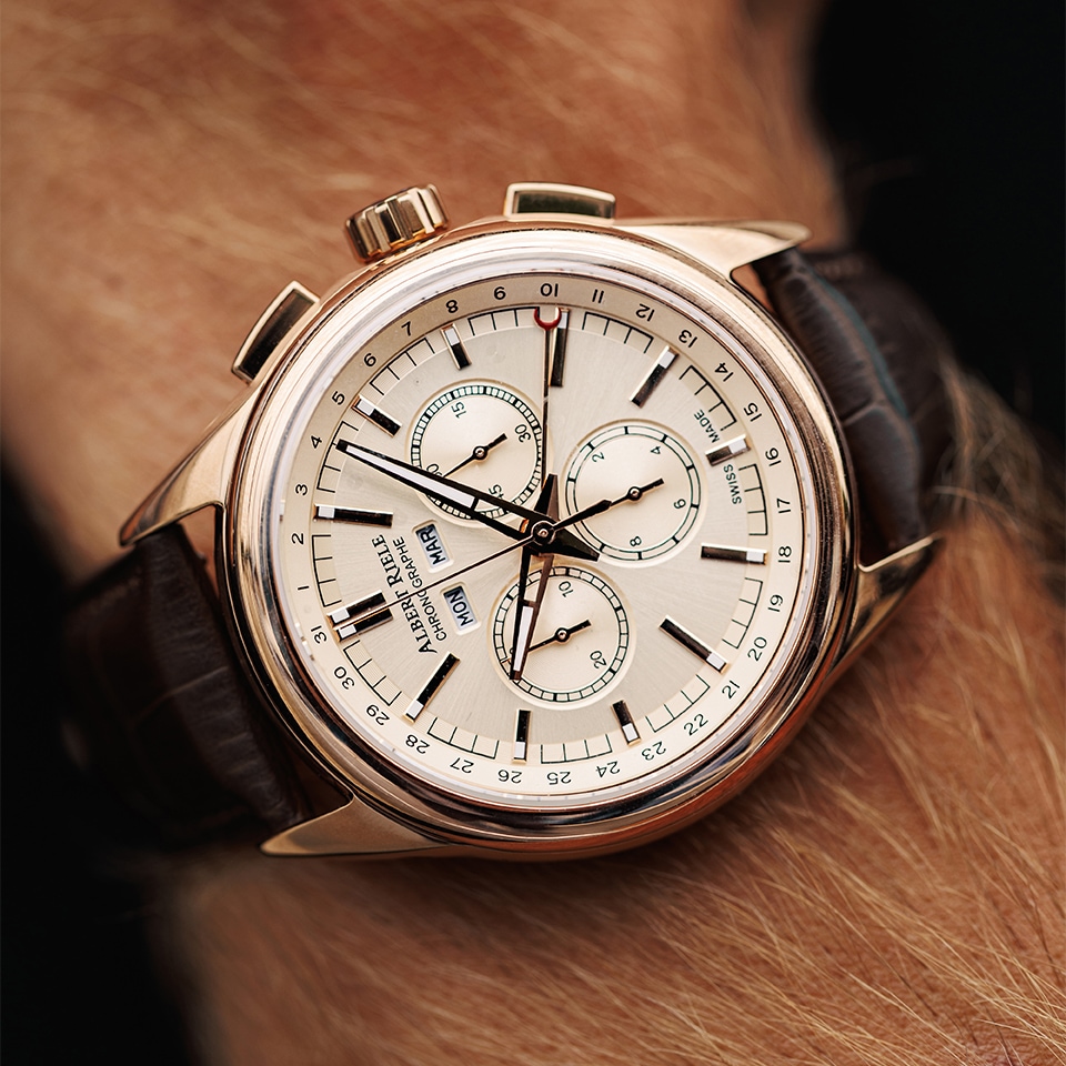 Elegancki zegarek z chronografem, jasną tarczą, kopertą w kolorze różowego złota i brązowym skórzanym paskiem prezentowany na nadgarstku