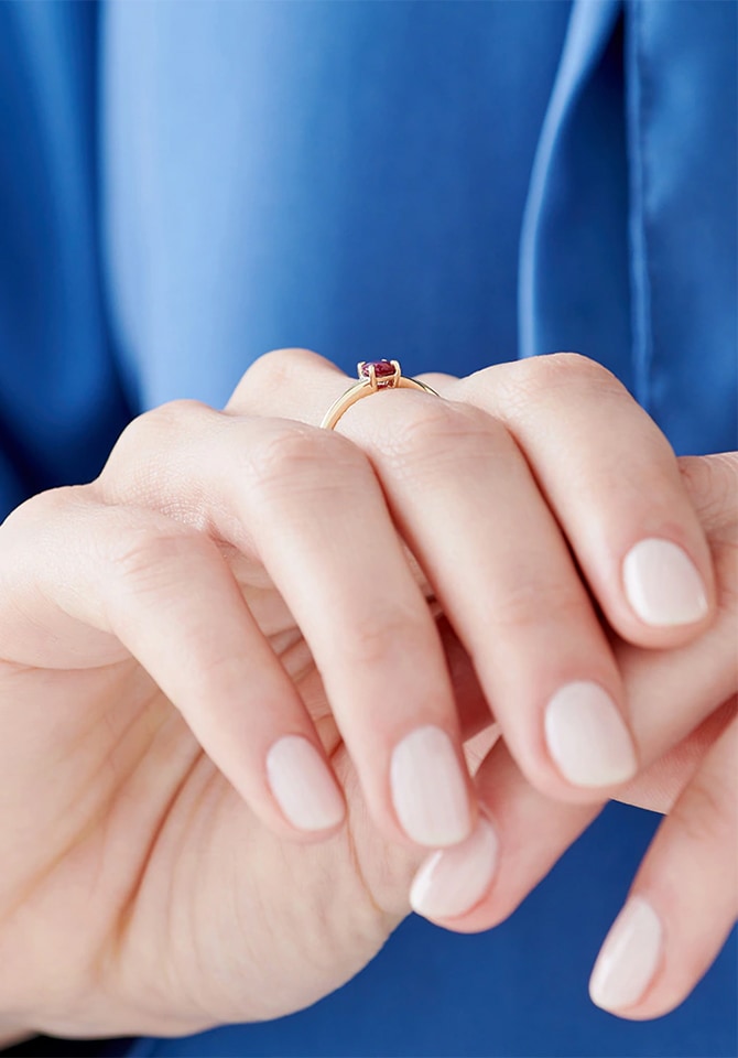 Dłonie z delikatnym pierścionkiem z czerwonym kamieniem i jasnym manicure