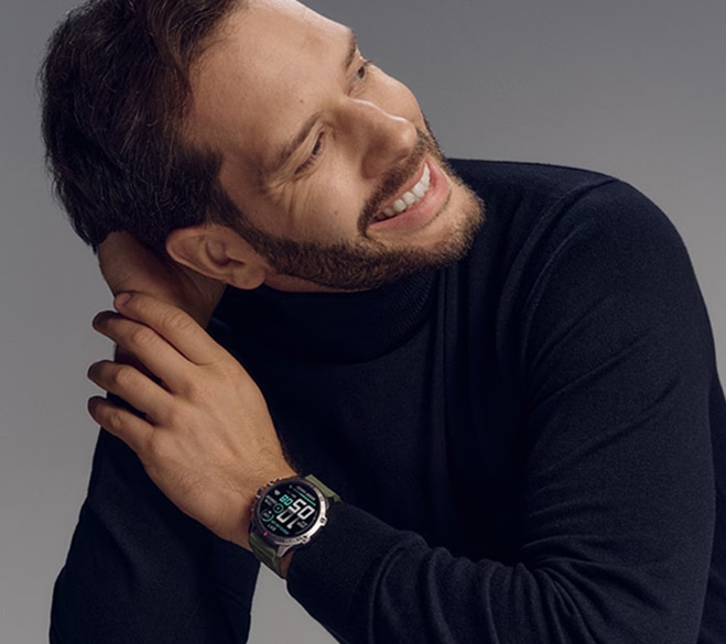 Mężczyzna o ciemnych włosach ubrany w czarny sweter - golf, prezentuje na nadgarstku smartwatch