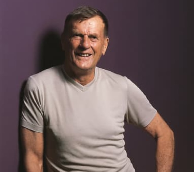 Uśmiechnięty Rolf W. Schnyder w jasnym t-shircie na fioletowym tle