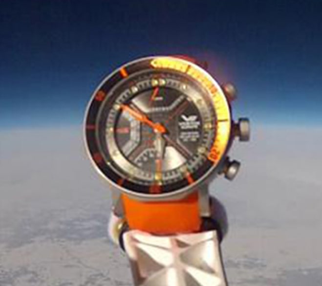 Zegarek marki Vostok Europe z pomarańczowym paskiem prezentowany na ziemskiej orbicie
